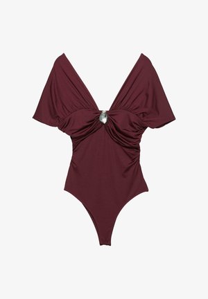 Burgundi egyberészes fürdőruha széles, vállról lelógó ujjakkal, ráncolt anyaggal a deréknál, és egy kör alakú ezüst díszítéssel a közepén.