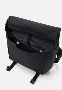 Borsa a messanger nera con chiusura a rotolo, divisori interni, fodera texturizzata, spallacci regolabili e hardware a fibbia.