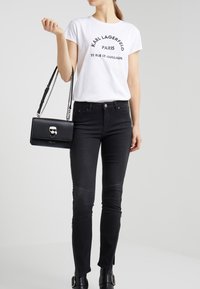 T-shirt bianco con testo stampato nero, jeans skinny neri con zip laterali e una borsa in pelle nera con dettaglio a teschio.