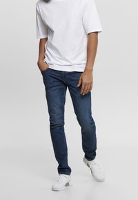 Modré džínové kalhoty s úzkým střihem, spojené s jednoduchým bílým tričkem a bílými síťovanými teniskami. Tento outfit má neformální a moderní vzhled.