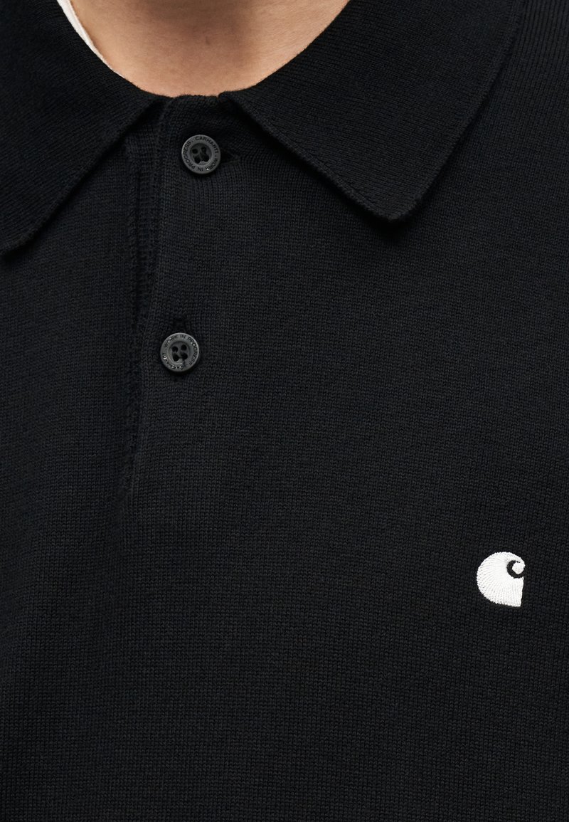 Schwarzes Strick-Poloshirt mit zwei schwarzen Knöpfen und einem kleinen weißen bestickten Logo auf der linken Brust.