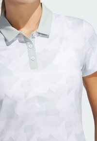 Polo shirt i lysegrå med et subtilt geometrisk mønster. Har en lysegrøn krave og en to-knaps lukning. Blødt, textured stof.