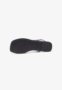 Svart platt sandal sula med en slät yta, något böjd form och texturerat gummimönster för grepp. Sömnadsdetaljer längs kanterna.