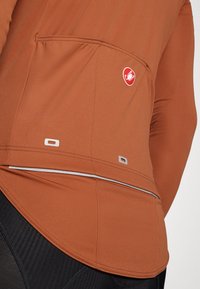 Veste de sport marron en tissu lisse, avec une poche au dos, des accents réfléchissants et un petit logo en haut à gauche.