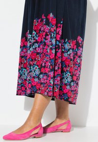 Maxikleid mit floralem Muster auf navy Hintergrund, mit lebhaften rosa und blauen Blumen am Saum, kombiniert mit flachen rosa Wildlederschuhen.