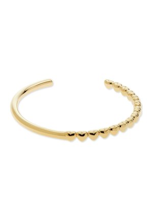 Bracelet jonc ouvert en or avec une rangée de petites perles en forme de cœur sur un côté, sur fond blanc.