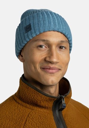 Blau gestreifte Strickmütze mit einem schwarzen Logopatch, kombiniert mit einer braunen Fleecejacke. Die Mütze hat eine weiche Textur und sitzt eng.