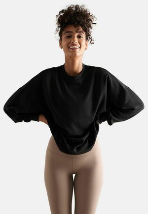 Schwarzer, übergroßer Sweatshirt mit runder Halslinie und herunterhängenden Schultern, kombiniert mit hellbeigen Leggings. Glatte Textur und bequeme Passform.