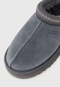 Tamno sivi zimski sloj UGG cipele na slip-on s mekanim unutrašnjim oblogom i dekorativnim pletenim ukrasom oko otvora za gležanj.