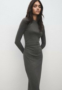 Figursyet, langærmet grå kjole med en glat tekstur og indsnørede detaljer i siden, der har en rund halsudskæring og et minimalistisk design.