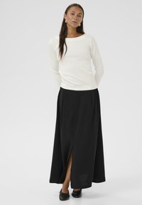 Un haut à manches longues blanc associé à une jupe maxi noire avec une fente avant, texture lisse et chaussures noires plates. Design simple et classique.
