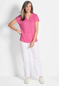 Roze v-hals top met korte mouwen, gedragen met witte uitlopende broek. Gestructureerde stof, casual pasvorm, gecombineerd met lichte sneakers.