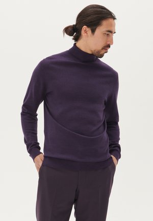 Dunkellila Rollkragenpullover aus weichem, strukturiertem Strick. Mit langen Ärmeln und einem taillierten Saum, kombiniert mit maßgeschneiderten dunklen Hosen.