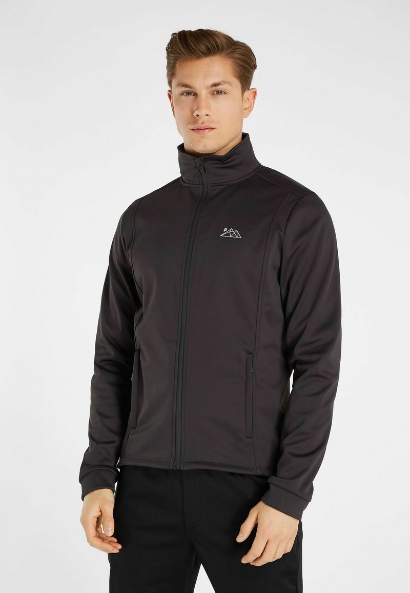 Donkergrijze softshell jack met hoge kraag, een rits aan de voorkant en zijzakken. Bevat een klein berglogo op de borst. Rekbare stof.