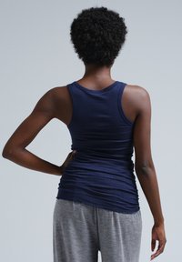 Canotta attillata blu navy realizzata in morbido cotone, con scollo rotondo e texture plissettata sul retro. Abbinata a pantaloni grigi larghi.