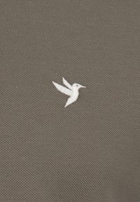 Tejido verde oliva con un patrón de punto texturizado que presenta un logo de colibrí bordado en blanco. Diseño simple, acentos mínimos.