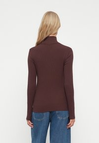 Hnedý dlhý rukáv turtleneck sveter s rebrovanou textúrou, priliehavým strihom a vysokým výstrihom, skombinovaný s voľnými modrými džínsami.