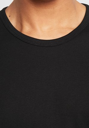 Zbliżenie na szyję i górną część klatki piersiowej osoby ubranej w czarną koszulkę z okrągłym dekoltem.