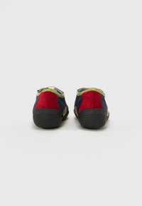 Zapatillas coloridas con paneles de ante en azul marino, rojo y verde, tejido texturizado, suela de goma y un diseño aerodinámico. Se muestra la vista trasera.