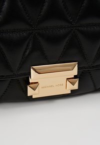 Černá kožená kabelka s prošívaným vzorem, zlatými kovovými detaily a obdélníkovou sponou s gravírováním "MICHAEL KORS".