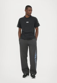 Black t-shirt with graphic accents on sleeves and logo on chest, paired with gray sweatpants featuring blue text design.