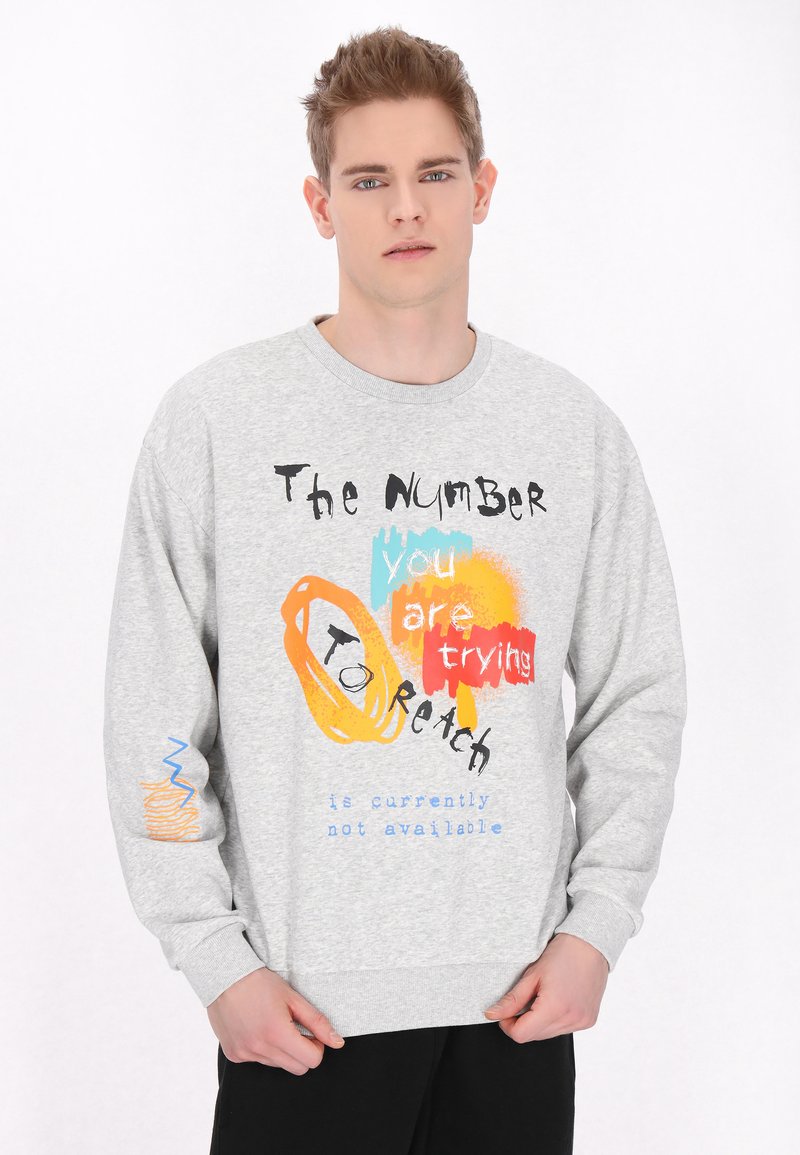 Sweatshirt gri cu un amestec de text stilizat colorat și forme grafice. Materialul pare moale, cu manșete și tiv cu nervuri.