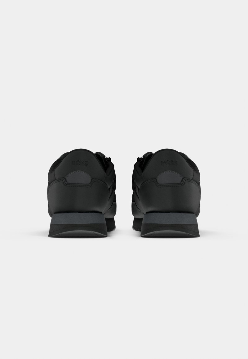 Chaussures de sport noires avec une tige synthétique lisse, une semelle en caoutchouc et un dos rembourré, présentant un logo ton sur ton au niveau du talon.