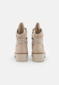 Bottines en cuir beige avec une texture douce et froissée, un bout arrondi, un petit talon et des sangles décoratives. Elles possèdent deux zippers latéraux pour la fermeture.