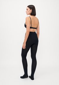 Sort bodysuit med justerbare stropper, sømløst design og tætsiddende silhuet, der har en glat tekstur og uigennemsigtig finish.
