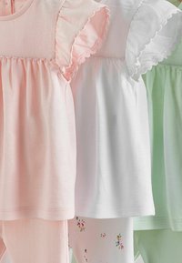 Trois tenues pour bébé avec des manches à volants en rose, blanc et vert menthe, chacune assortie à un pantalon ou un legging assorti.