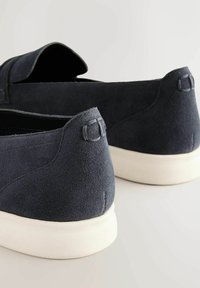 Námornícke semišové topánky na slip-on s hladkým povrchom, bielou gumovou podrážkou a šitými detailmi na zadnej strane, s malým slučkovým akcentom.