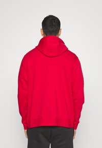 Rød hættebluse med en afslappet pasform, som har en stor hætte og ribbede manchetter. Stoffet ser blødt og glat ud, velegnet til daglig brug.
