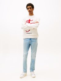 White sweater with red graphic design and "tommy jeans" text, paired with light blue jeans and white sneakers. Casual fit and style.