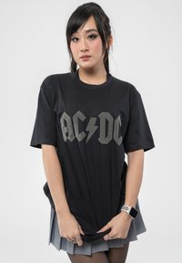 Black cotton t-shirt featuring bold gray "AC/DC" logo with lightning bolt, relaxed fit, short sleeves, and round neckline.