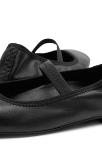 Bailarinas de cuero negro con una pequeña correa elástica, textura suave, puntera redondeada y costuras detalladas en los bordes.