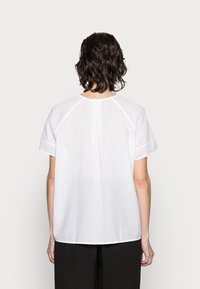 Witte, textuurvolle blouse met korte mouwen, ronde halslijn, rugplooidetail en een ontspannen pasvorm. Geen zichtbare hardware of patronen.