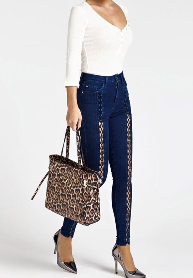 Jeans bleu foncé avec des découpes sur les côtés, un haut blanc à manches longues et un sac fourre-tout à imprimé léopard. Des talons gris pointus complètent le look.