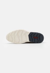 Semelle de chaussure de sport avec un schéma de couleurs crème et marine, dotée d'un motif texturé et d'un design hexagonal pour une meilleure adhérence.