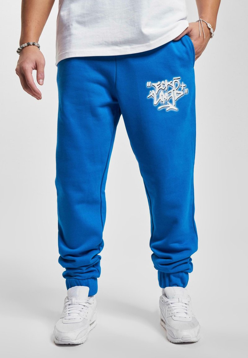 Blauwe sweatpants met een geborduurd wit grafisch ontwerp in graffiti-stijl. Afgewerkt met elastische boorden en een zachte, gladde textuur.