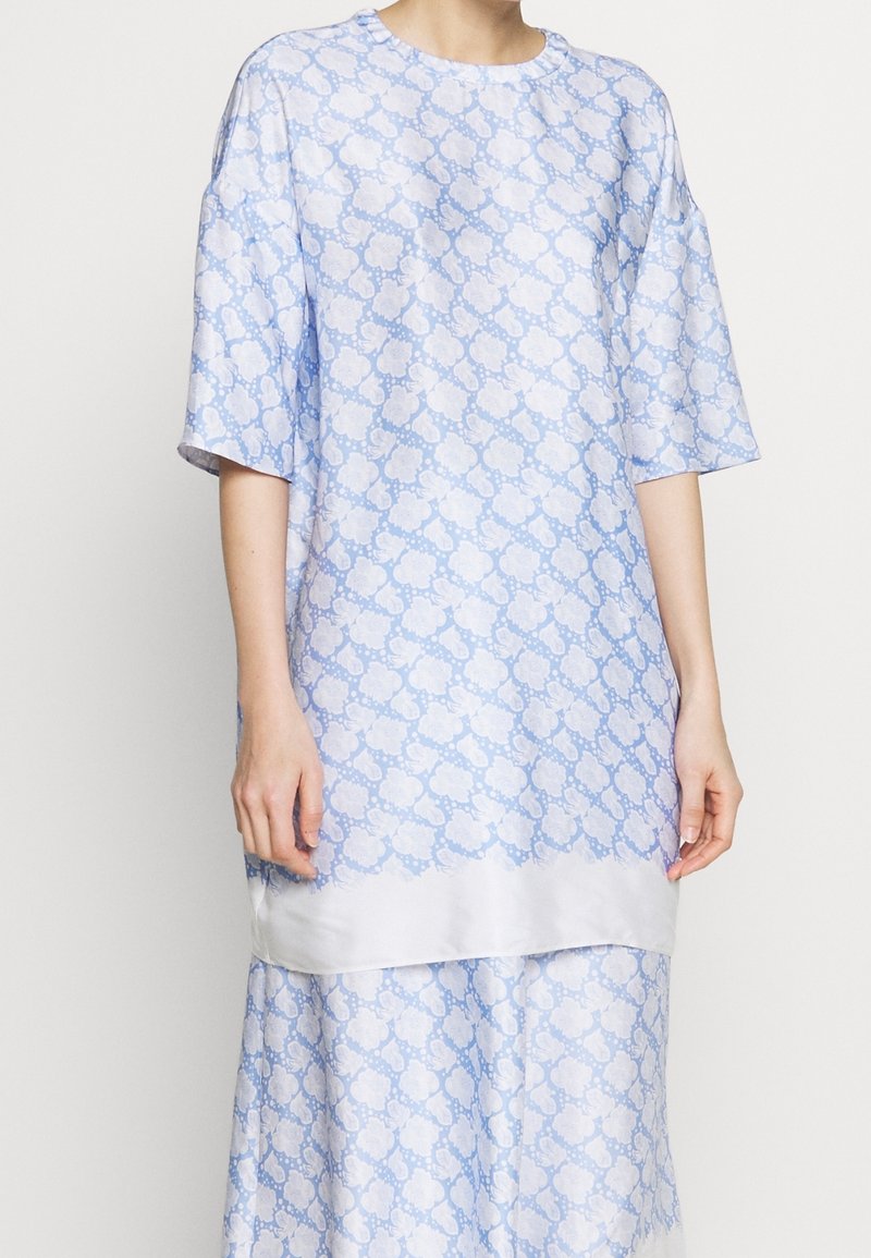 Vestito azzurro chiaro con un motivo floreale, maniche corte, scollatura rotonda e una texture liscia simile alla seta.
