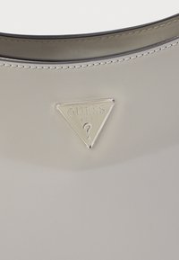 Borsa grigia con finitura lucida, una targhetta logo triangolare in argento e dettagli cuciti lungo il bordo superiore.