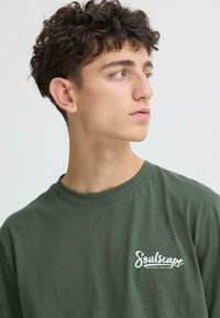 T-shirt en coton vert avec un col rond, arborant un logo blanc "Soulscape" sur la poitrine. Coupe décontractée et douce avec des manches courtes.