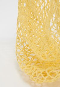 Gele netzak gemaakt van geweven garen, met een open ontwerp, flexibele textuur en een afgeronde vorm, geschikt voor het dragen van spullen.
