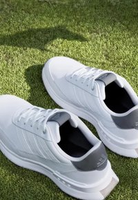 Sneaker bianche da ginnastica con tomaia in sintetico liscia, dettagli grigi texturizzati sul tallone e una suola spessa e texturizzata.