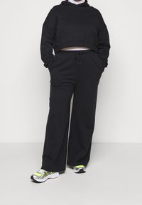 Czarna krótka bluza z długimi rękawami, zestawiona z luźnymi czarnymi joggerami. Posiada sznurek w talii oraz subtelną teksturę, noszona z sportowymi sneakersami.