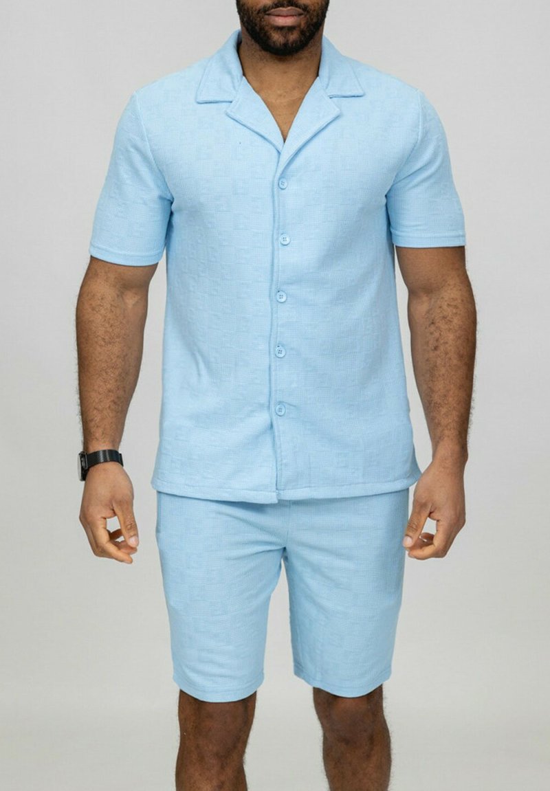 Chemise à manches courtes bleu clair et shorts assortis en tissu texturé. Présente un col et une fermeture à six boutons sur le devant.