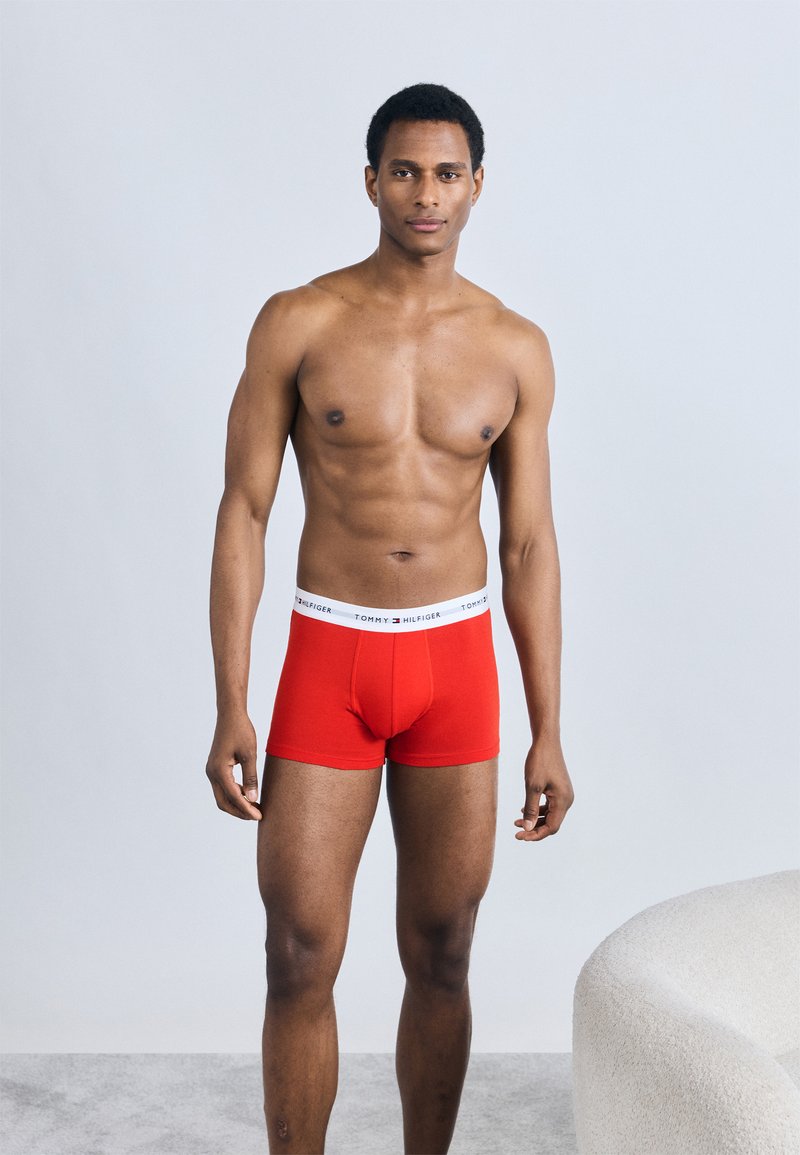 Κόκκινα βαμβακερά μποξεράκια με λευκή μέση που φέρει την ετικέτα "TOMMY HILFIGER." Το μοντέλο στέκεται όρθιο, παρουσιάζοντας τη γραμμή και το σχέδιο.