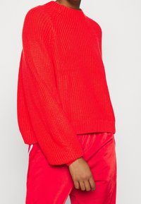Rode gebreide trui met een ronde halslijn en lange, licht oversized mouwen. Ribbelzoom en gestructureerde stof. Draagt met bijpassende rode onderstukken.