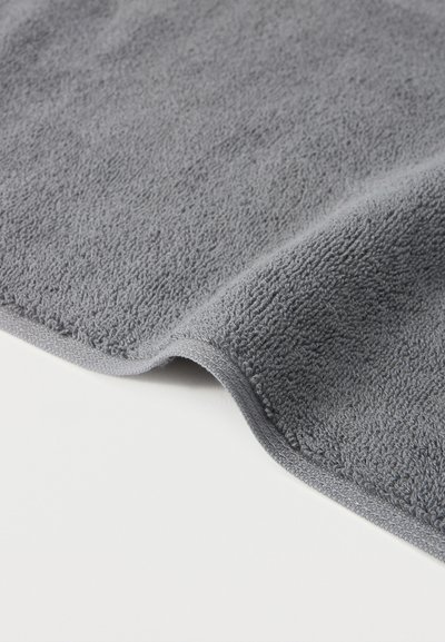 Μαλακό γκρίζο ύφασμα πετσέτας με διπλωμένη άκρη, απλωμένο σε λευκή επιφάνεια.