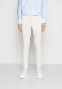 Białe, wąskie spodnie z gładkiego materiału; do tego jasnoniebieska koszula w paski na guziki oraz białe tenisówki.